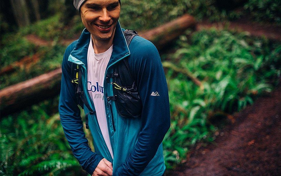 A man zipping up a coat in the woods. 