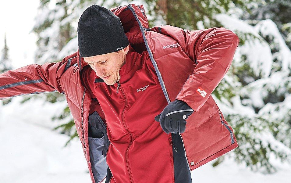 A man putting on a Columbia Outdry coat in a snowy forest.