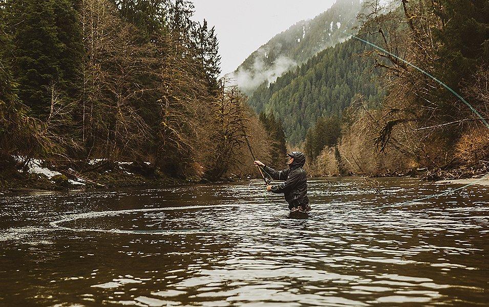 Pro angler Curtis Ciszek stands in the river casting a fly rod on a cold, rainy day.