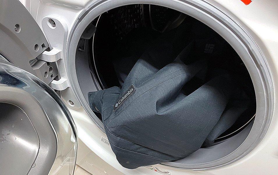A ski jacket is pictured in a dryer with the door open.  