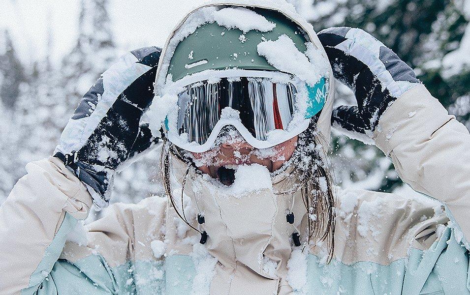 A skier covered in snow looks at the camera smiling.