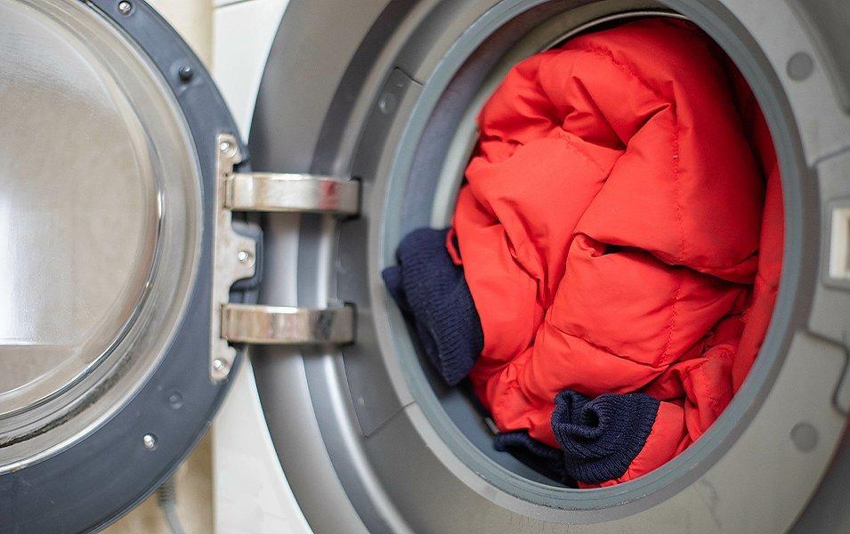 A  red puffer jacket sits in a washing machine with the door open. 