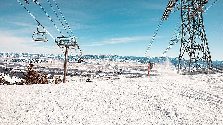 A skier mid jump on a run in a resort, in between two chair lifts
