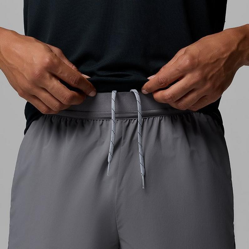A man lifting his shirt to reveal the drawstring-adjustable waistband of his grey shorts.