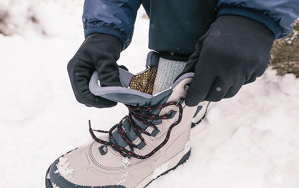 A winter camper ties his hiking boots in the snow. 

 