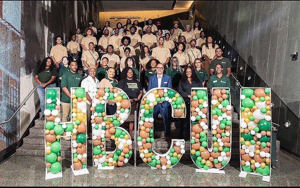 A group of staff and volunteers from Greening Youth Foundation stand in front of a sign filled with balloons that says “HBCUI.”