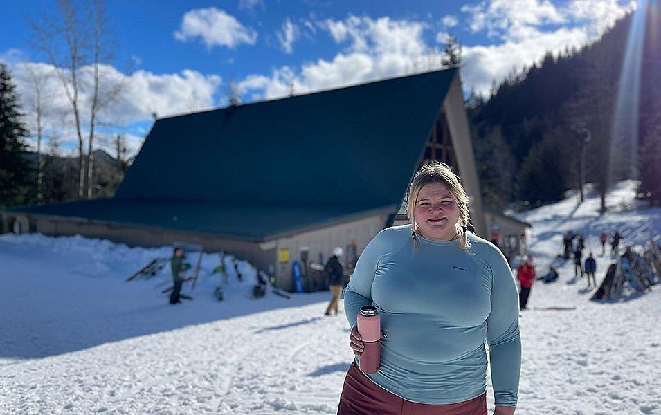 Snoqualmie ski patroller Annet Soot stands near a ski lodge holding a pink thermos and wearing a blue Columbia Sportswear baselayer top.