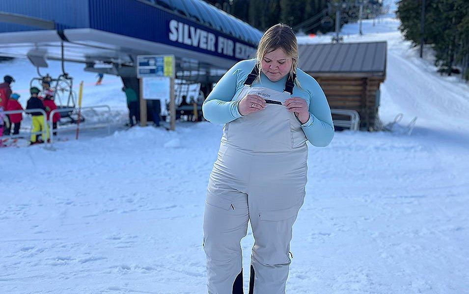 Snoqualmie ski patroller Annet Soot stands in front of a chairlift wearing a light blue Columbia Sportswear baselayer top with white ski bibs. 