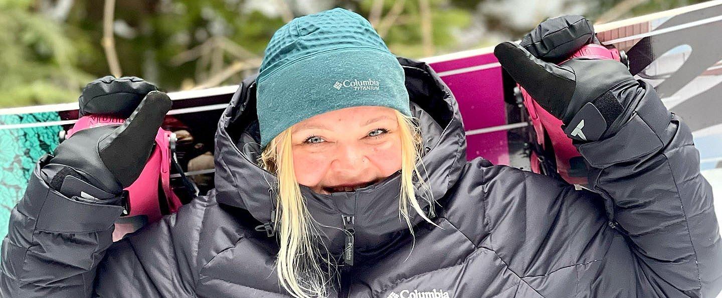 Snoqualmie ski patroller Annet Soot holds her snowboard behind her head and smiles at the camera.  
