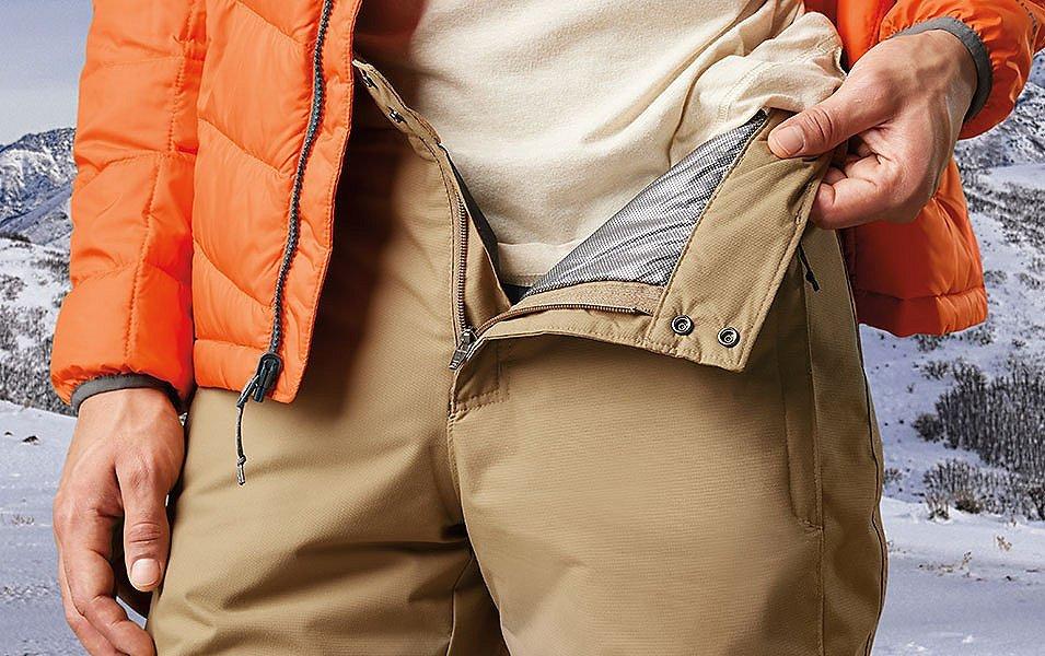 A skier stands in a snowy landscape folding back the zipper of his Columbia Sportswear ski pants to reveal a warm Omni-Heat liner.  
