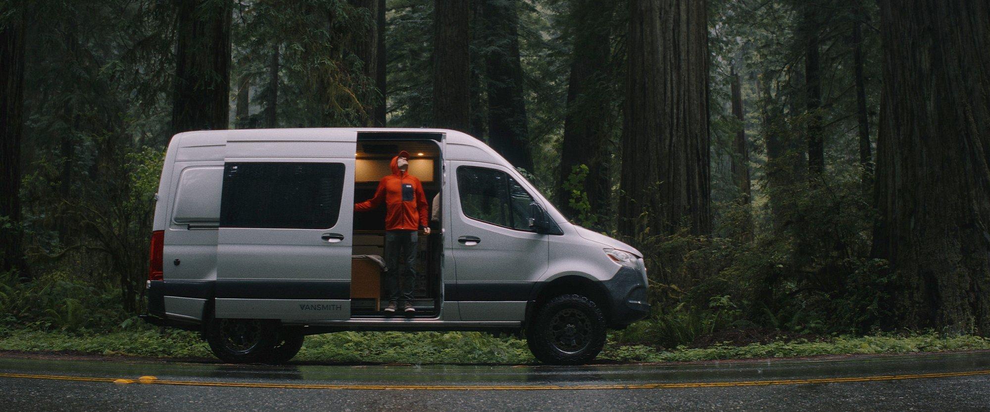 Still frame from the film: MHW Athlete Ethan Pringle, standing in his sprinter van, taking in the view of the giant redwood trees that surround him.