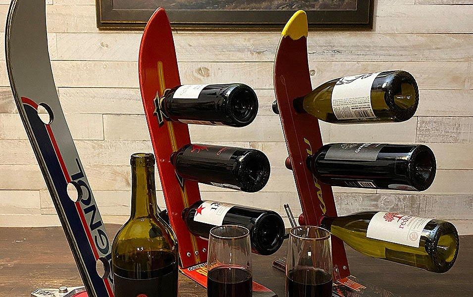 A collection of wine racks made from old skis sit on a table next to a couple of glasses of wine.  