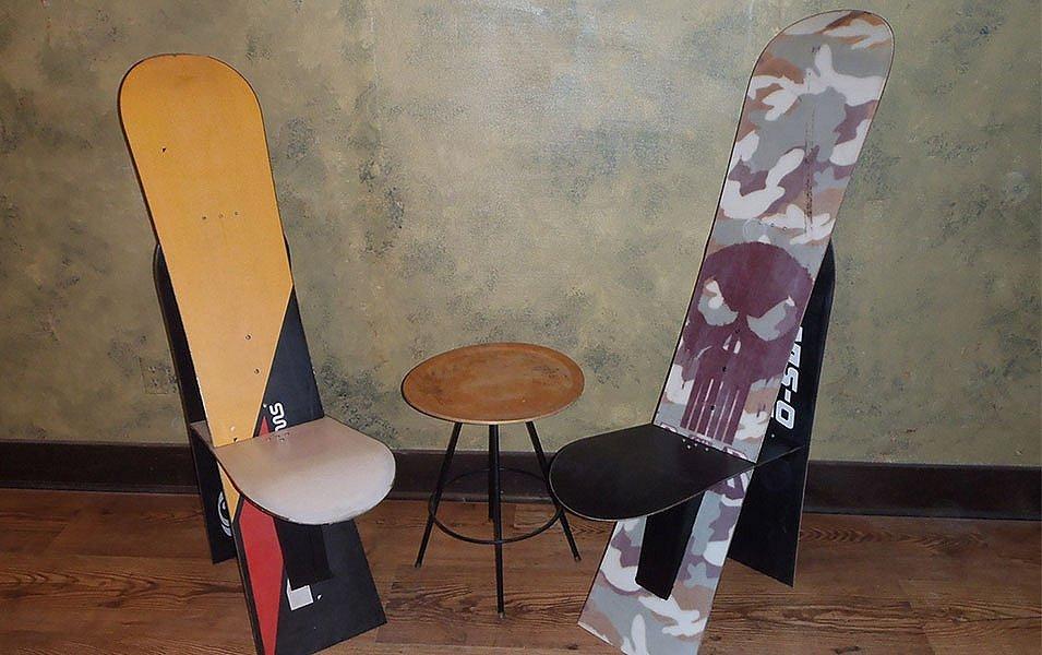 Two high-back seats made from recycled snowboards sit next to a small coffee table on a wood floor. 