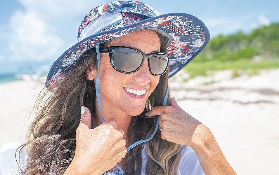 A girl wearing a colorful Columbia Sportswear booney hat stands on the beach and smiles ear to ear. 