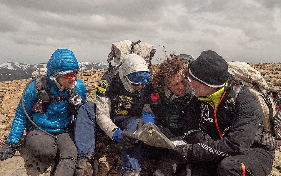 Four people huddled around a map on a high rocky ridge.