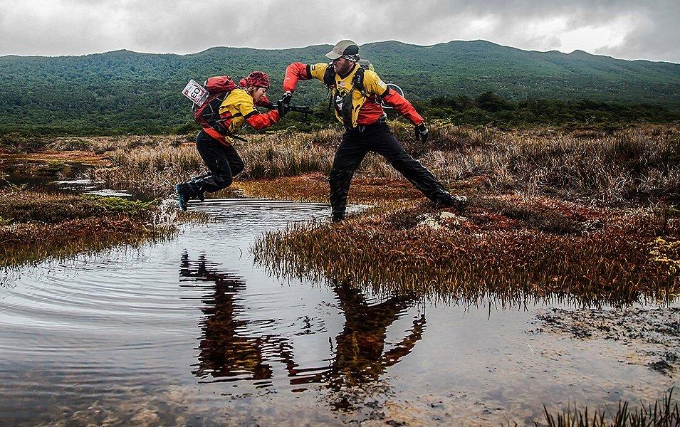 A man helping a woman jump over a stream. 
