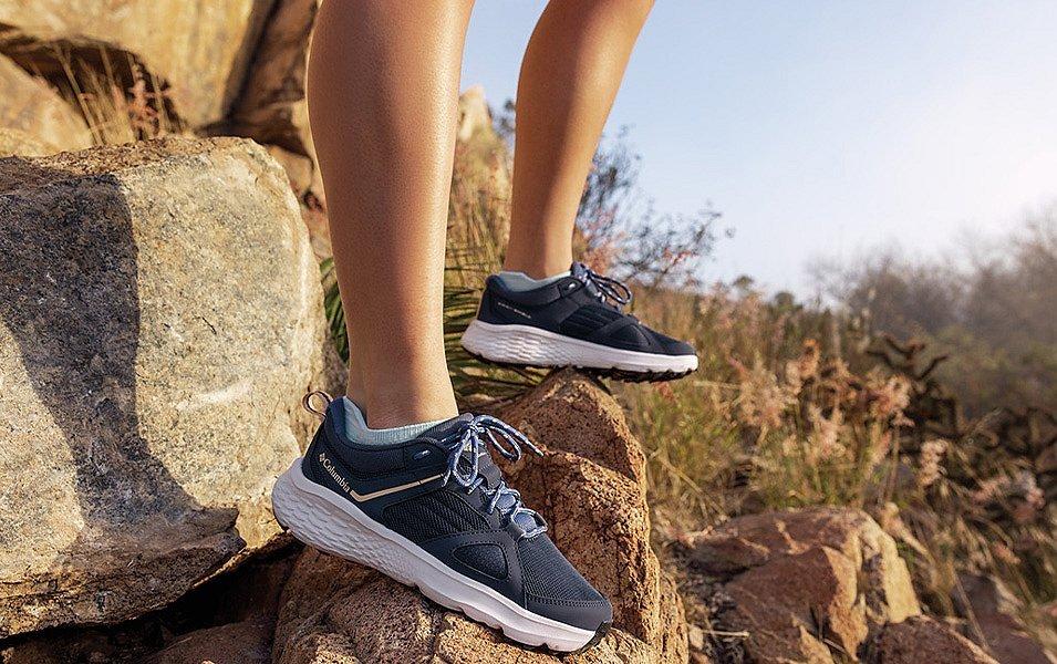 A close-up image of two feet standing on rocks by tall grass in an area prone to mosquitoes. 