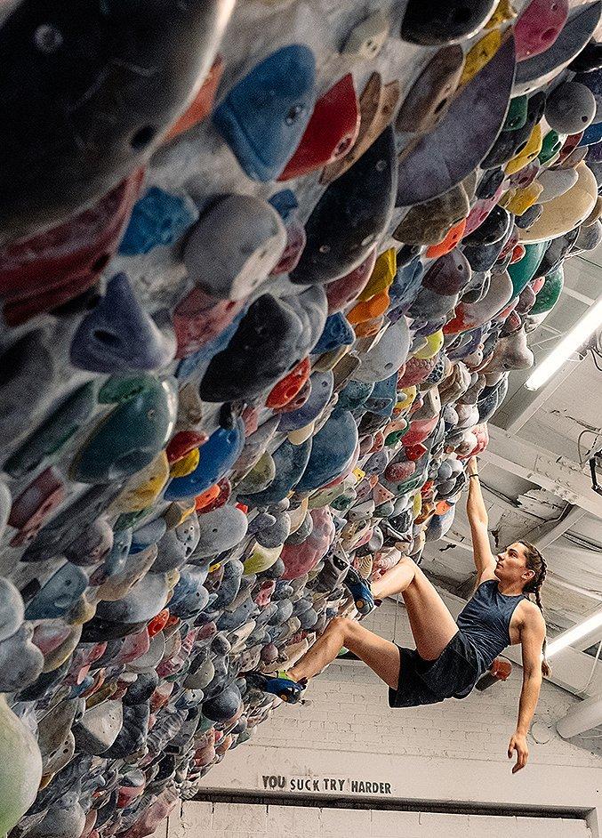 Kyra Condie bouldering in her home climbing gym in Minneapolis, making good progress on the route, with her personal mantra, "you suck try harder" on the wall in the background.