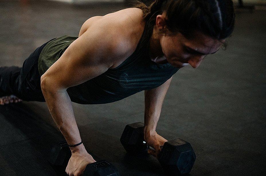 Kyra Condie doing pushups on the ground, holding on to two big weights.
