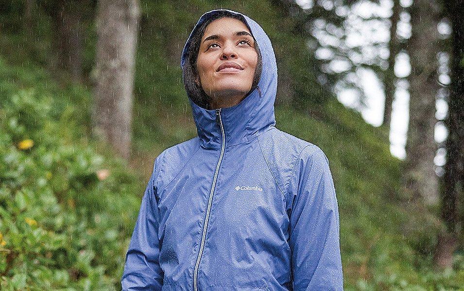 Femme portant une veste de pluie Columbia Sportswear sur un sentier de forêt pluvieuse.