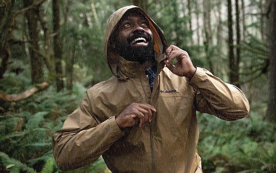 Homme dans une forêt pluvieuse portant une veste de pluie marron clair Columbia Sportswear.