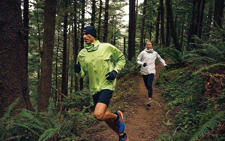 Man and a woman running on a forest trail. 