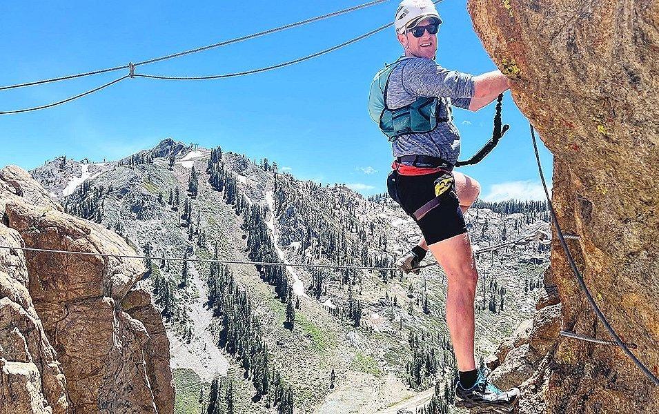 Professional trail runner Willie McBride is pictured rock climbing on a sunny day with a beautiful landscape behind him. 

 