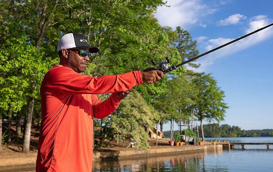 Mark Daniels Jr. casting his line into the water while wearing Performance Fishing Gear on a sunny day along a shoreline.