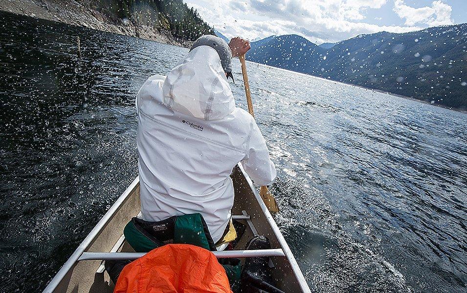 A man wearing a white Columbia Sportswear OutDry™ Extreme jacket paddles away from the camera in a canoe. 