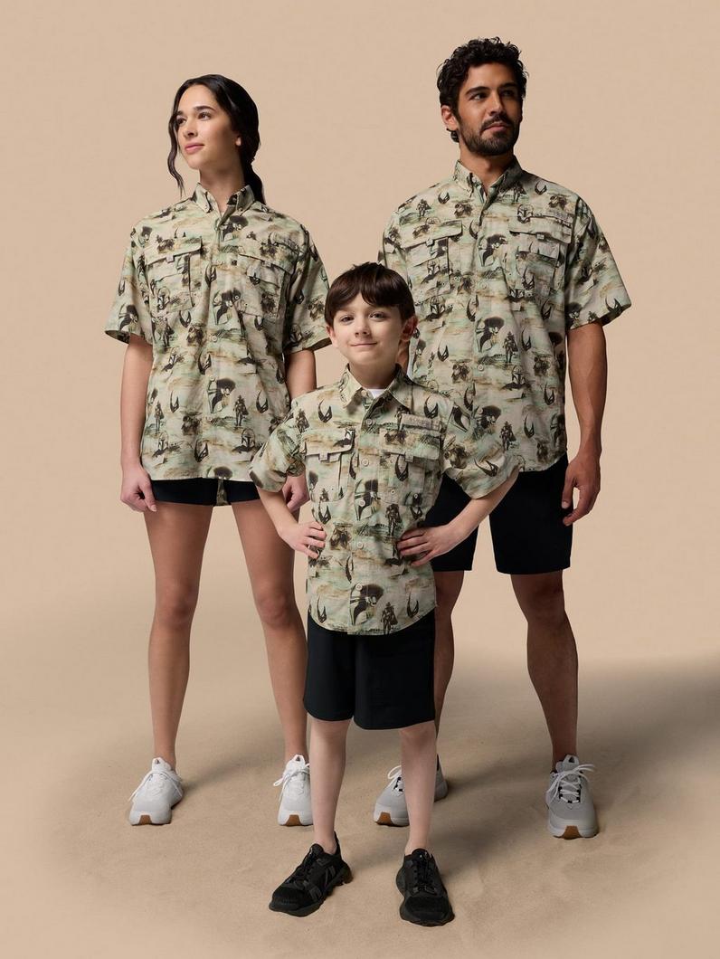 Three people wearing matching short-sleeved button-up shirts with western-themed print and black shorts.