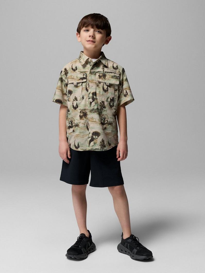 Boy wearing short-sleeve button-up shirt with desert scene print and black shorts.