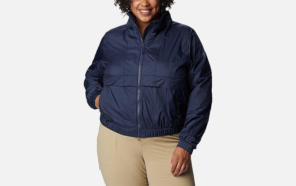A woman models a light orange Columbia Sportswear Sunny City Windbreaker Plus Size with a white background.