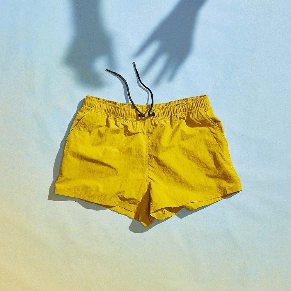 Laydown of the Stryder shorts on a gradient background with shadow hands lingering over the shorts.