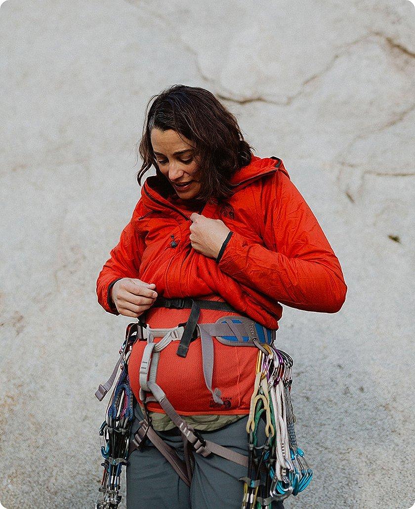 Miranda looking down at her pregnant belly, with climbing harness on