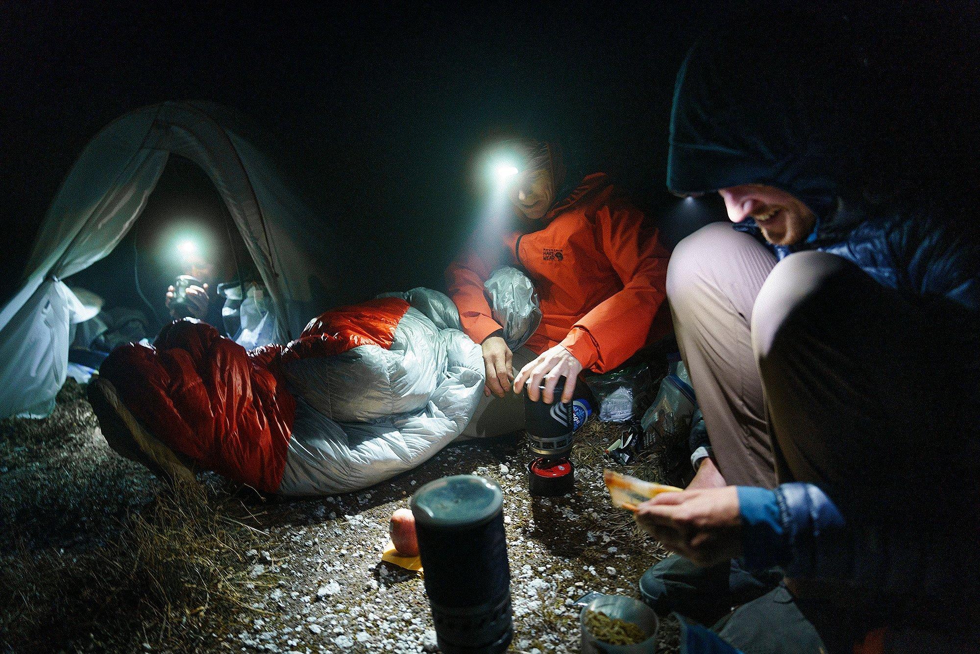 Camping at night scene, making dinner at the jet boil, everyone has headlamps on.