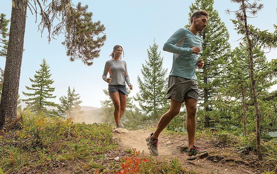A trail runner wearing UPF-rated clothing runs down a path with a woman jogging behind him. 