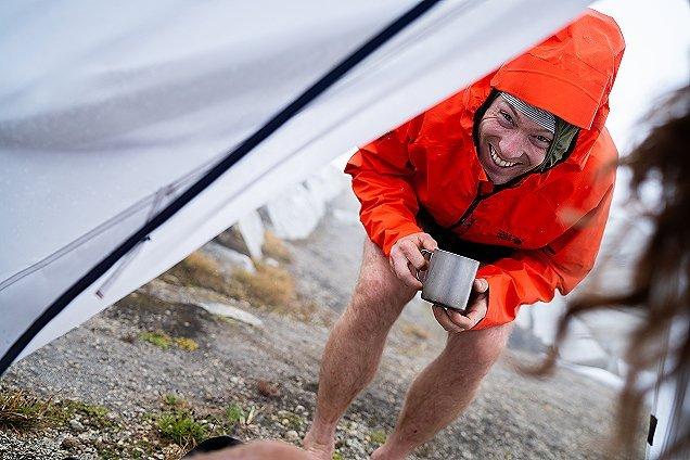 CJ smiling with a cup of coffee in his rainjacket.