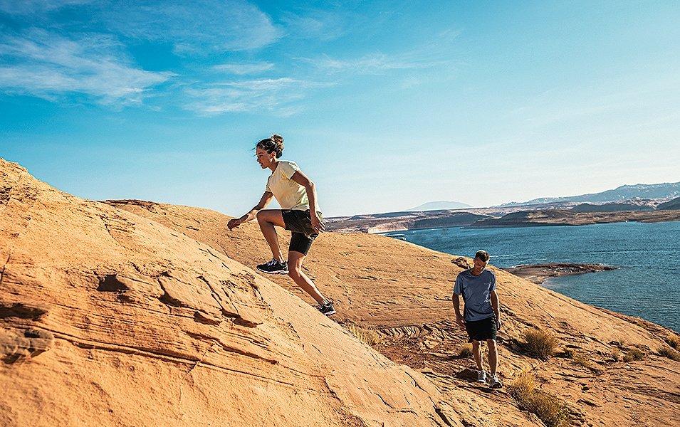 Two hikers climbing on rocky ridge over looking a lake. 