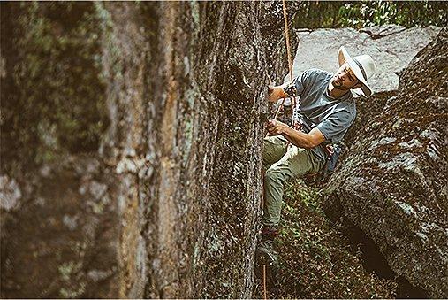 Josh is repelling and examing the rock in a harness, looking for the best route up.