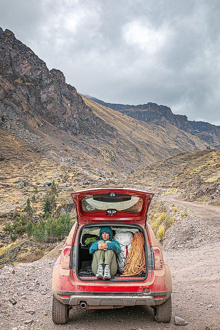 Charlotte sitting in the back of their SUV, next to her pack and rope, in the Chacco Huayllascca Valley.
