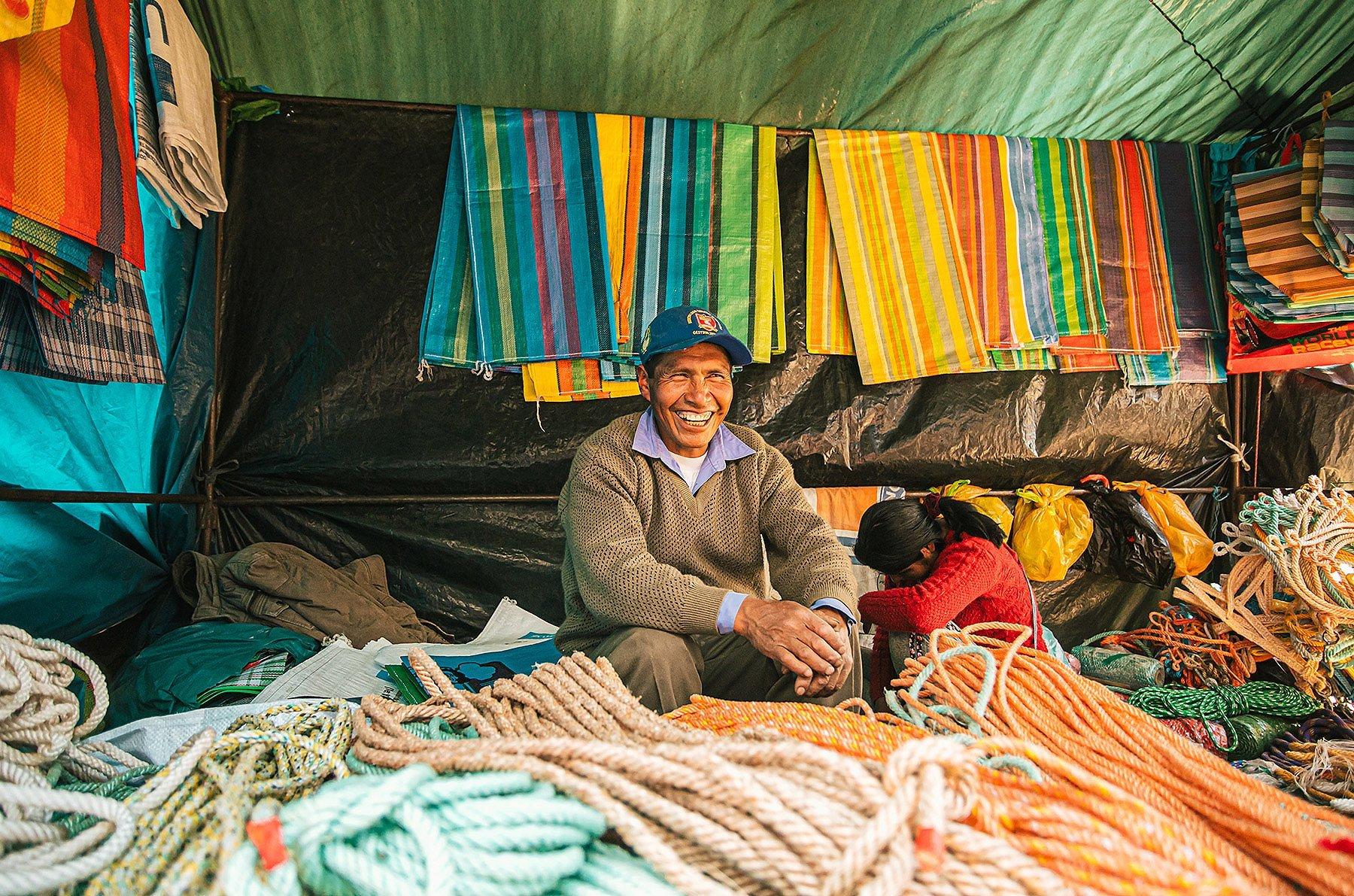 At the farmers market in the center square of Pitumarca, Peru, a man sits in his booth with all kinds of rope and material for sale.