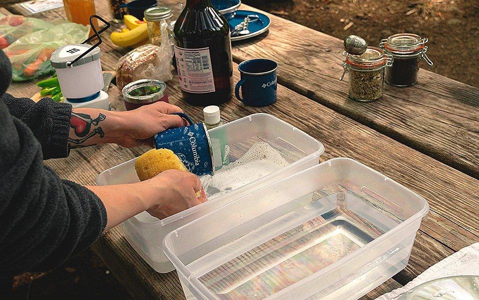 People doing dishes on a picnic table. 