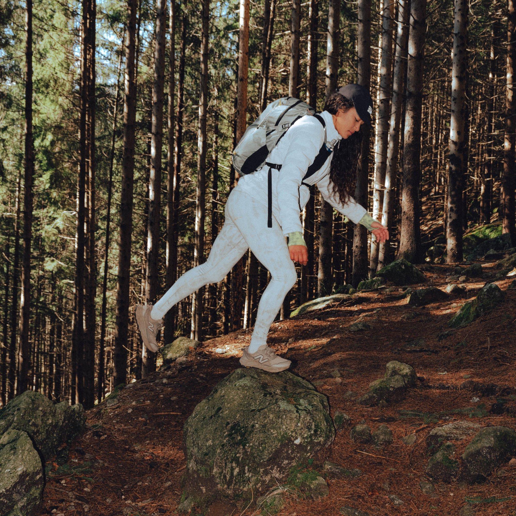 Professional ultrarunner Alexa Romano playfully hops up and balances on a large rock on the trail.