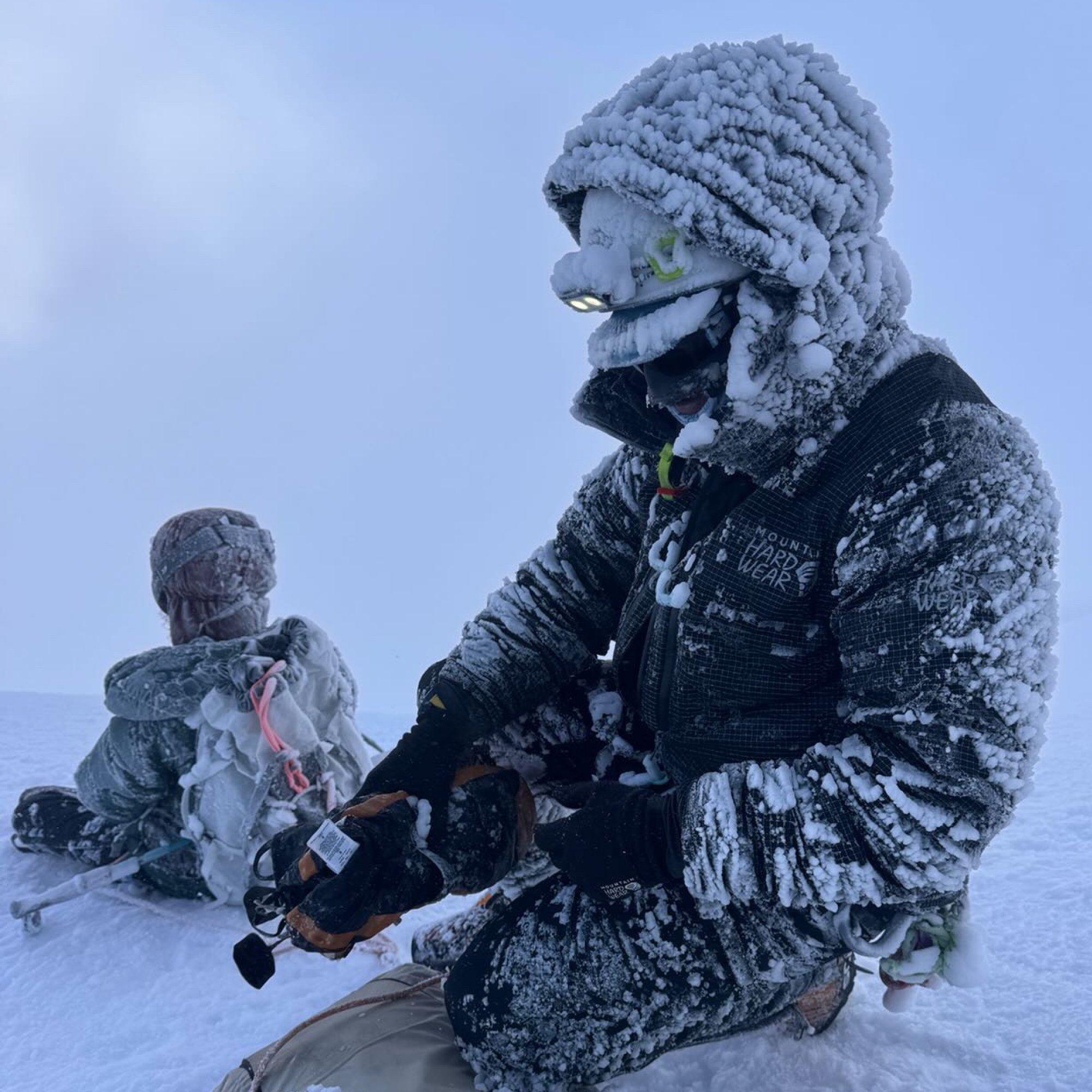 Completely crusted in ice and snow, professional mountaineer Benny Lieber crouches in the flurry to stow his gear.
