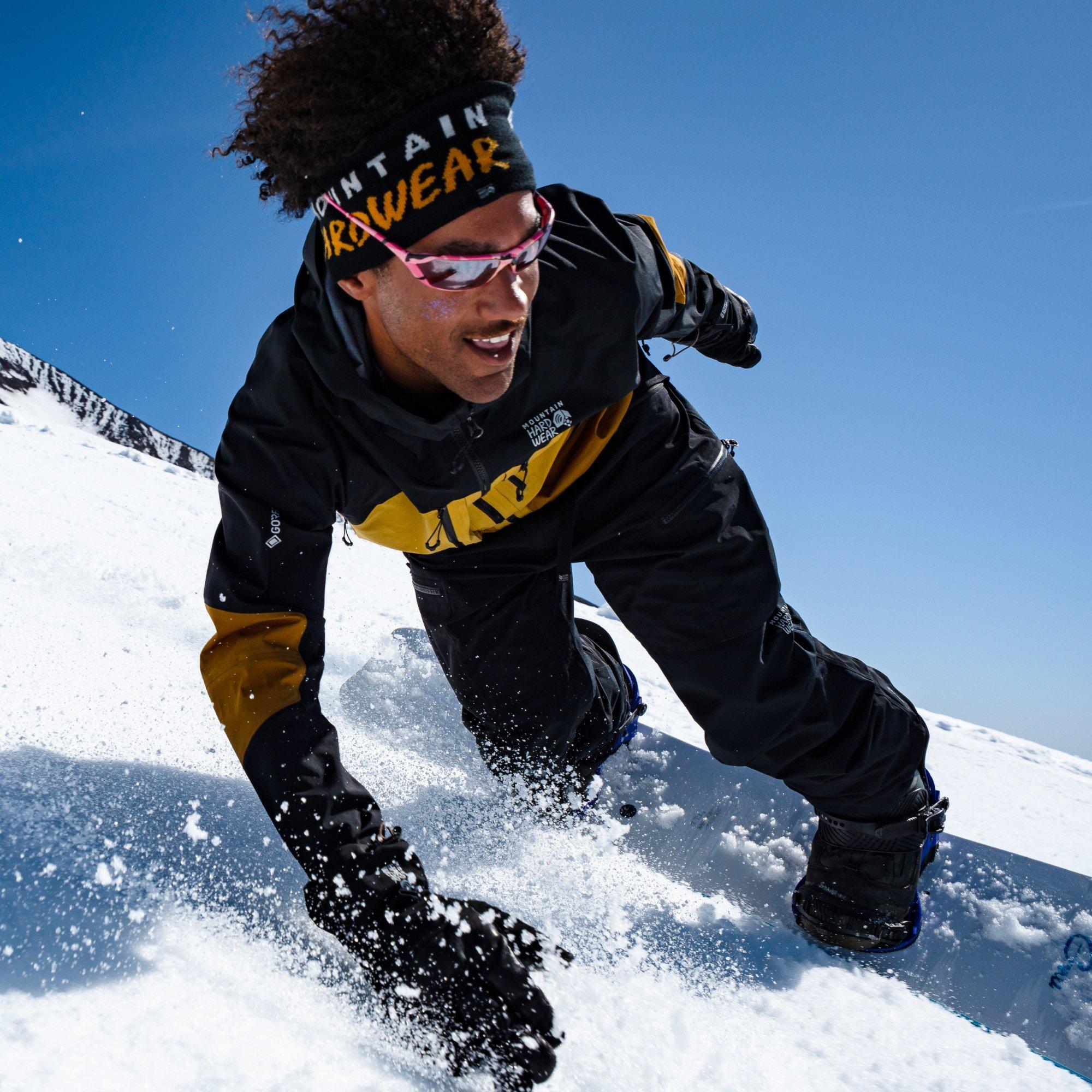 Professional snowboarder and guide Bryce Barnes flies past the camera beaming, his hand mittened hand skimming the ground.