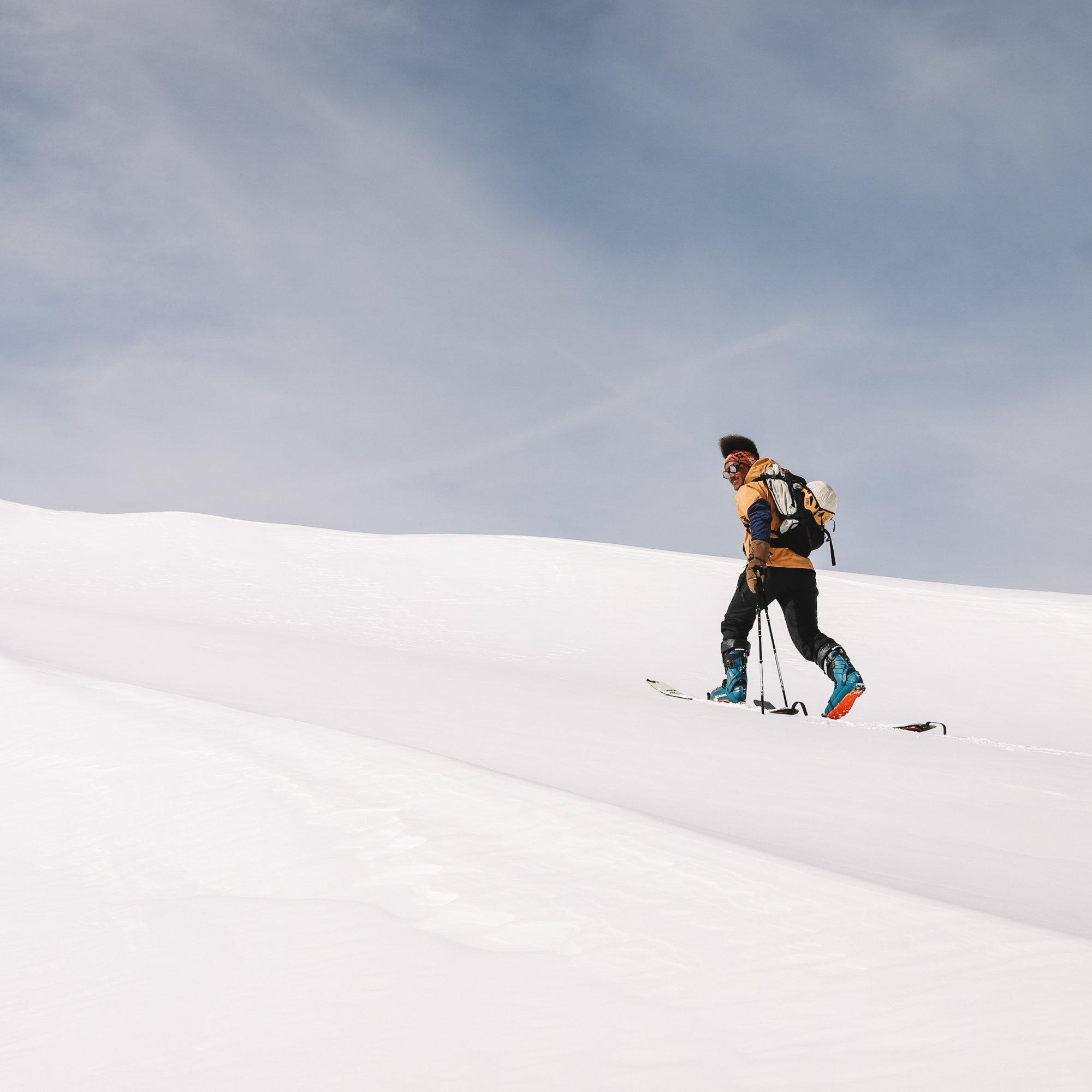 Using a split board with skins and poles, professional snowboarder Bryce Barnes makes his way up the mountain.