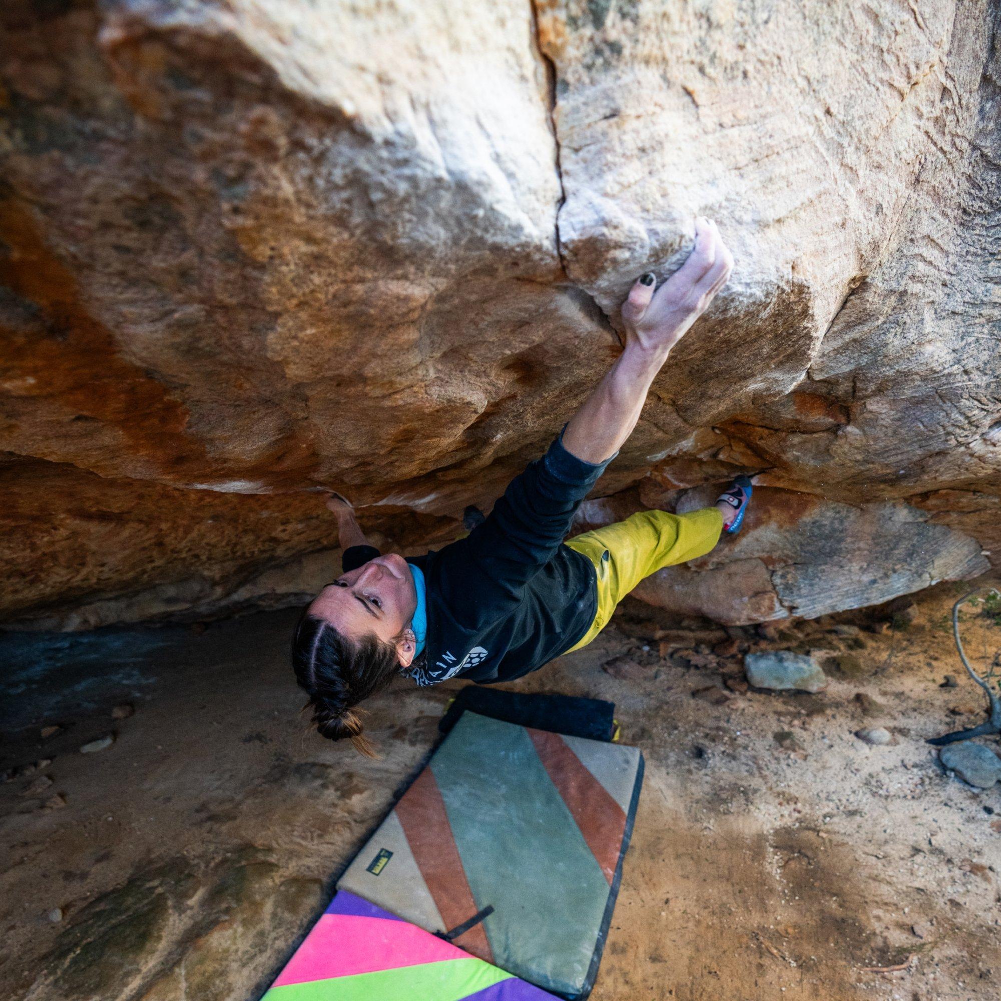 Crash pads below, professional climber Kyra Condie mantles an overhang, her chalky fingers gripping the outer edge.