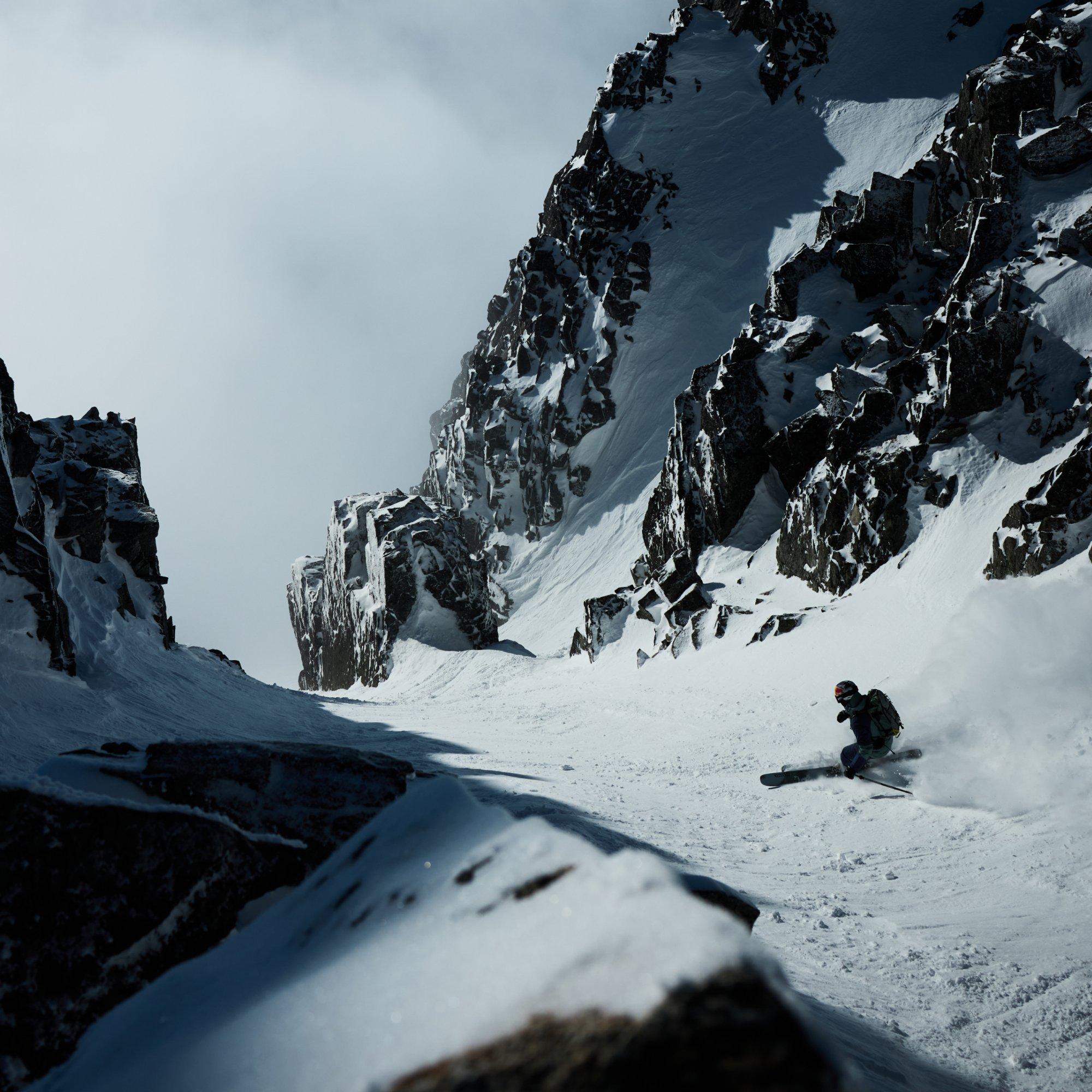 Framed by dark, jagged rocks, professional skier Manon Loschi kicks up snow as she carves her way down a chute.