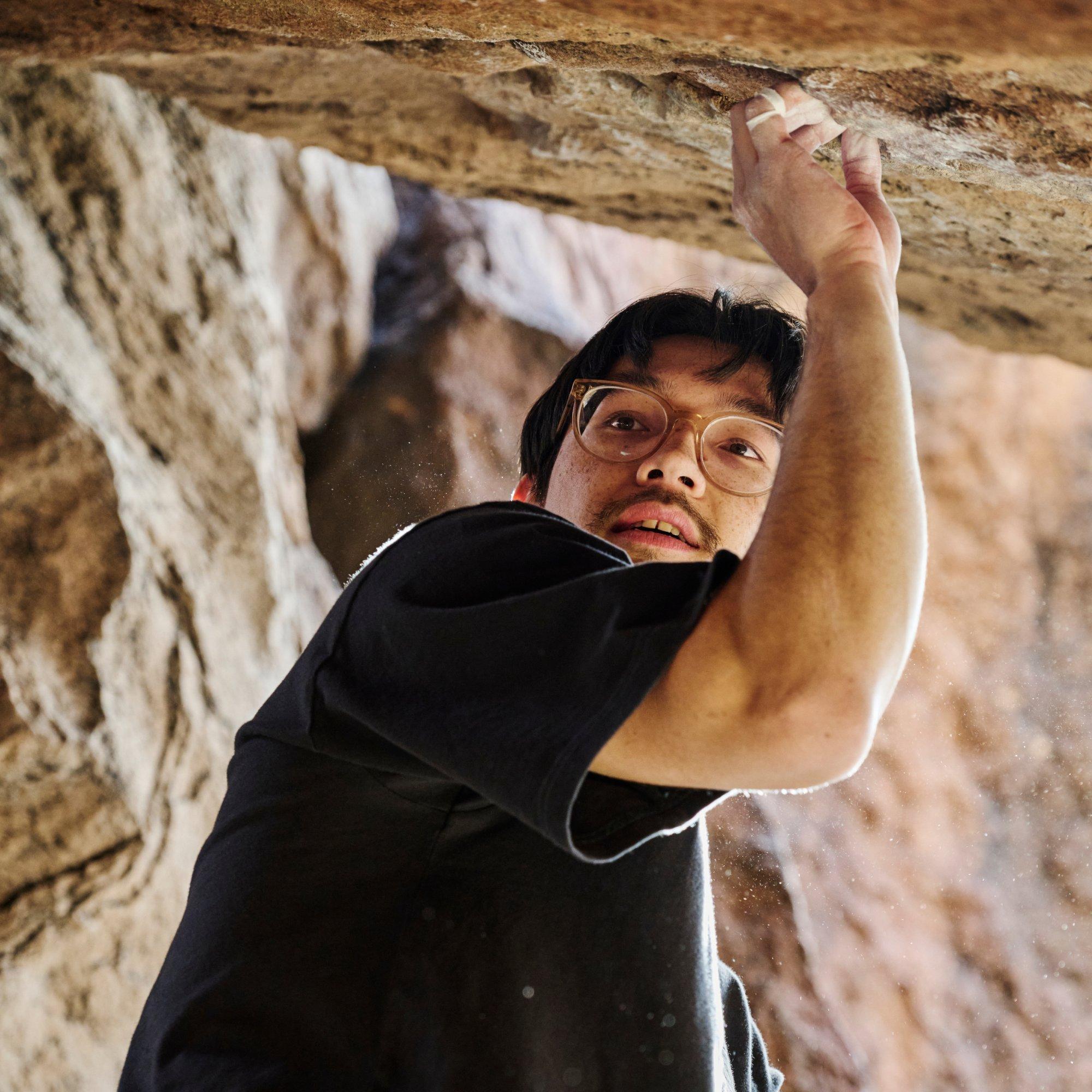 Under a ledge with taped fingers in the rock, professional climber Noah Wheeler pauses and looks over his shoulder.