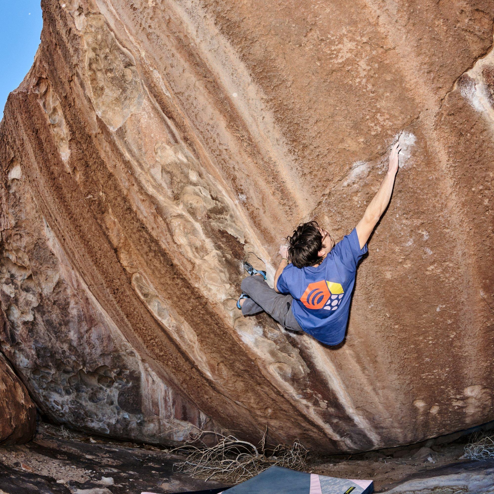 Crash pads below, professional climber Noah Wheeler reaches for a chalky finger crack while bouldering.